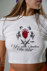 Remera crop top de algodón elastizado color blanco, con diseño gráfico estampado en el centro que incluye un corazón anatómico y texto. Presenta cuello redondo y mangas cortas.