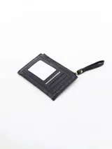 Billetera blanca con textura de cocodrilo, cierre de cremallera superior y un bolsillo frontal con solapa y botón a presión. Incluye una correa lateral para la muñeca.