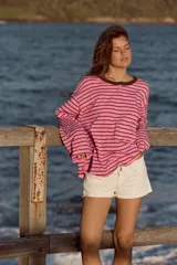 Camiseta estilo panadera de manga larga, con diseño a rayas horizontales en color rosado y marrón. Presenta cuello redondo con ribete marrón a contraste y cierre frontal parcial con tres botones pequeños.