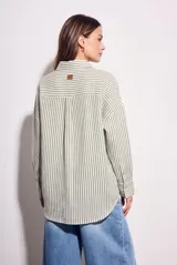 Camisa de corte oversize con estampado de rayas verticales, cuello clásico, cierre frontal con botones y bolsillo en el pecho. Presenta mangas largas con puños abotonados y un diseño fluido.