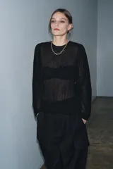 Blusa negra de manga larga abullonada, con tejido plisado y cuello redondo con abertura y botón en la espalda.