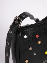 Cartera bandolera color crema de símil cuero, con apliques frontales de tachas redondas de colores y estrellas plateadas. Tiene correa regulable con hebillas y cierre superior con cremallera.