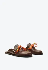 Zueco mocasín de cuero marrón, con taco plano, hebilla metálica dorada lateral y detalle de cordón naranja con cuentas decorativas en el empeine.