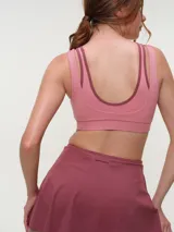Top deportivo rosa con efecto layering, escote redondo bajo y tirantes dobles. Presenta el logo de la marca en tono oscuro en el frente.