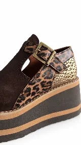 Guillerminas de cuero marrón chocolate, con detalles en animal print y textura dorada metalizada. Presentan una tira con hebilla metálica en el empeine, aberturas laterales y suela de plataforma corrida con franjas en contraste.