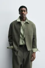 Sobrecamisa de corte boxy fit confeccionada en tejido compacto color beige, con cuello solapa, cierre frontal de botones y bolsillos laterales en costura.