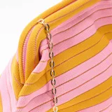 Bolso bandolera de diseño estructurado tipo saco, con patrón de rayas horizontales en tonos amarillo mostaza y rosado. Cuenta con cierre de broche metálico superior y correa de cadena dorada.
