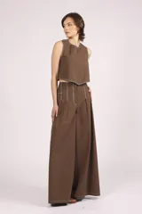 Pantalón marrón de corte palazzo, tiro alto, con pliegues frontales y pespuntes blancos decorativos.