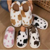 Pantuflas sin talón confeccionadas en algodón afelpado y piel sintética, con divertido estampado de manchas de vaca en tonos blanco y marrón, y suela de PVC.