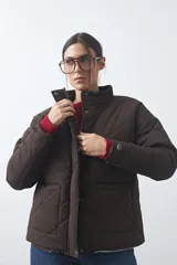 Campera acolchada de nylon color marrón, con cuello alto, cierre frontal con botones a presión y bolsillos delanteros. El interior cuenta con forro de corderito para mayor abrigo.