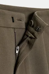 Pantalón de tiro medio con pinzas delanteras, bolsillos laterales y falsos bolsillos de vivo en la parte trasera. Presenta un corte holgado que se estrecha hacia el tobillo, con bajo acabado en pliegues y cierre frontal con cremallera, botón interior y gancho.