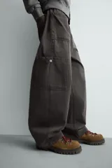 Pantalón de corte relaxed fit confeccionado en algodón, color gris oscuro. Presenta bolsillos delanteros, bolsillos laterales tipo cargo en las perneras y cierre frontal con cremallera y botón.