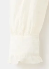 Blusa de tejido semitransparente color crudo, con diseño recto, cuello alto con volados, mangas largas abullonadas con puños abotonados y detalle de bordado floral en toda la prenda. Cuenta con cierre frontal de botones ocultos y ribete con volado en la botonera.