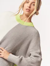 Buzo tejido oversized con bloques de color blanco y gris, cuello redondo en verde neón, tajos laterales y flecos verdes en las mangas.