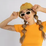 Gorro tipo bucket color mostaza con efecto desgastado y pequeño bordado de flor naranja en la parte frontal.