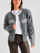 Cárdigan de punto gris con diseño jacquard en la parte superior, cuello redondo y cierre frontal con botones. Presenta puños y ruedo acanalados.