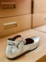 Zapato tipo Mary Jane plateado de cuero, con correa al tobillo con hebilla y tachas plateadas.