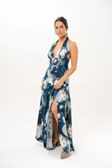 Vestido largo con escote halter profundo y diseño sin mangas. Presenta un estampado difuminado en tonos azules, celestes, blancos y grises, con corte ajustado en el torso y una falda larga con vuelo.