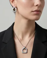 Set de joyería compuesto por un collar con cadena de eslabones y dije cuadrado con centro circular, y aros colgantes a juego con el mismo diseño geométrico. Realizado en acero inoxidable con acabado pulido.