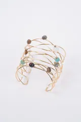 Brazalete rígido de diseño abierto, elaborado en alambre dorado entrelazado con pequeñas piedras naturales de diversos colores incrustadas.