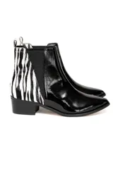 Bota tipo chelsea con diseño combinado. Presenta la parte delantera en cuero vacuno charolado negro y la parte trasera en cuero con estampado animal print tipo cebra. Cuenta con elásticos laterales negros y taco cuadrado bajo.