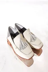 Mocasines color blanco hueso con detalle de borlas plateadas y talón en cuero plateado.