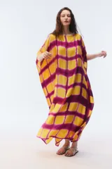 Kaftan maxi amplio de color amarillo, con escote redondo, mangas cortas y ruedo irregular. Presenta un diseño estampado a cuadros con efecto teñido.