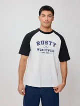 Remera blanca con mangas raglán negras y estampado frontal con el logo de Rusty en azul.