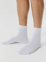 Kit de tres pares de medias unisex de caño medio, confeccionadas en tejido suave y elástico de color blanco, con el logo de la marca estampado en la planta del pie.