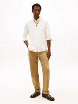 Chomba de manga larga Tommy Hilfiger color blanco, de corte regular y tejido de algodón suave. Presenta cuello clásico, cierre frontal parcial con cremallera y ribetes tricolores, además del logo bordado en el pecho.