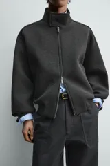 Cazadora de corte relajado confeccionada en tejido técnico compacto con elasticidad. Presenta cuello subido con cierre de botonadura oculta, cierre frontal con cremallera, bolsillos de vivo en la cadera y bajo con rib elástico.