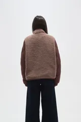 Campera de diseño híbrido que combina paneles de corderito sintético en color crema con mangas y bolsillos de tela técnica acolchada en color verde militar. Presenta cierre frontal completo, cuello alto y un pequeño parche decorativo en el pecho.