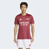 Camiseta de calentamiento Adidas del Arsenal FC, color bordó con estampado de rayas verticales sutiles. Presenta cuello redondo, logo de Adidas y escudo del club en contraste blanco, con tecnología Aeroready para mayor transpirabilidad.