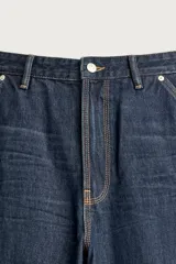 Pantalón jeans relaxed fit de mezclilla azul oscuro, con estilo carpintero que incluye bolsillos laterales y presillas de herramientas. Cuenta con costuras pespuntadas en contraste y cierre frontal con botón y cremallera.