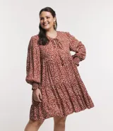 Vestido corto amplio color ladrillo con lunares irregulares color crema, cuello redondo con lazo, mangas largas con puños anchos y bajo fruncido.