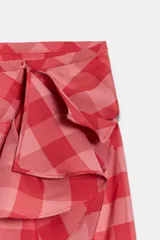 Falda midi de tiro medio, con estampado a cuadros vichy en tonos rojo y rosado, detalle de volantes en el delantero y cierre lateral con cremallera oculta.