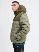 Campera puffer con capucha, diseño bicolor en tonos verde oliva, cierre frontal completo y bolsillos laterales. Presenta textura acolchada sin costuras visibles en el cuerpo y puños ajustables con velcro.