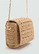 Bolso tipo bandolera de tamaño mini, confeccionado en fibras naturales tejidas con diseño de espiga. Presenta cierre de solapa con botón magnético, detalles de tachas metálicas en los bordes, forro interior y asa larga de cadena metálica dorada.