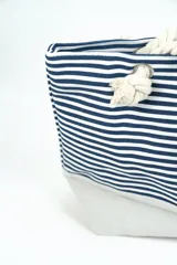 Bolso tipo tote marinero con estampado de rayas horizontales azul marino y blancas, con base en tono crudo y asas de soga gruesa con nudos decorativos.