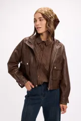 Campera corta de cuero sintético en color beige, con diseño de calce relajado, cierre frontal metálico, bolsillos con solapa en el frente y cordón ajustable en el ruedo.