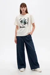 Remera de algodón de corte holgado, cuello redondo y manga corta, con estampa frontal abstracta de flores en tonos oscuros sobre fondo claro.