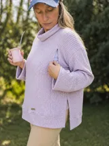Polerón de punto texturizado color lila, con cuello alto tipo polera, mangas largas y aberturas laterales con cierre. Diseño holgado con detalle de placa metálica en el ruedo.