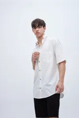 Camisa de manga corta en tela de algodón color blanco con rayas verticales en relieve y bolsillo en el pecho.