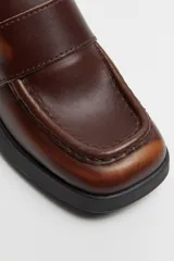 Mocasín de cuero color marrón con suela track negra y tacón bloque.