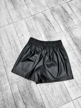 Short pollera negro de efecto cuero, con diseño cruzado en el frente y cintura alta.