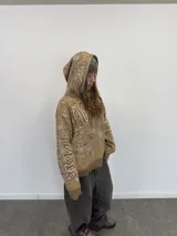 Buzo tipo hoodie con cierre frontal completo, confeccionado en tejido de punto grueso de algodón con diseño gráfico abstracto y tipográfico. Presenta capucha con bordado, puños y ruedo acanalados, y etiqueta de marca en la manga.