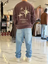 Buzo oversize de cuello redondo en color marrón con efecto gastado, con gran estampado en la espalda de estrellas y el texto VCP CNPT.