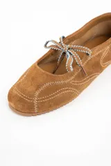 Chatita de gamuza color camel con costuras decorativas en hilo blanco y cordones ajustables en la parte superior. Presenta suela de goma dentada y tirador en el talón.