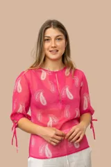 Blusa fucsia de gasa estampada con arabescos blancos, corte irregular y mangas 3/4 con lazos.