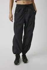 Pantalón jogger negro de inspiración utility, confeccionado en tejido liviano de poliamida. Cuenta con cintura elástica ajustable con cordón, bolsillos cargo con broches metálicos, diseño con paneles fruncidos y puños elastizados.
